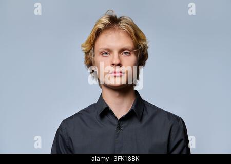 Porträtaufnahme eines ernsten jungen Mannes mit blondem Haar, der ein schwarzes Hemd trägt, vor hellgrauem Studiohintergrund stehend. Ideal für Business, Prof Stockfoto