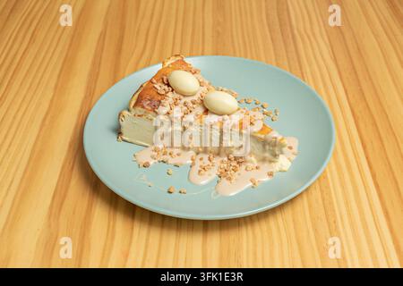 Gebackener Käsekuchen mit weißer Schokoladen-Eier, knusprigen Pralinenkrümeln und Karamell-Zuckerguss auf einem blaugrünen Keramikteller. Stockfoto