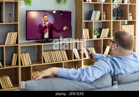 Übergewichtiger Mann mit Fernbedienung, der zu Hause auf dem Sofa entspannt und fernsieht Stockfoto