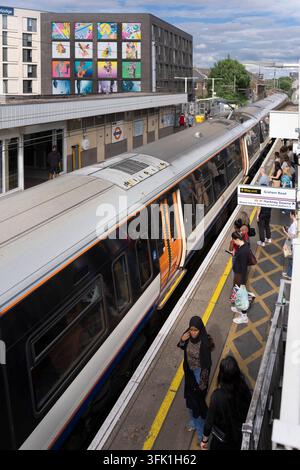 Pendler warten auf einen London Overground-Zug am Bahnhof Hackney Central, mit den farbenfrohen Kunstwerken am Travelodge-Gebäude im Hintergrund. Stockfoto
