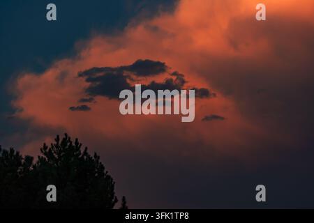 Dramatischer Sonnenuntergangshimmel mit dunklen Gewitterwolken, die lebendige orange und rote Wolken überlagern. Stockfoto