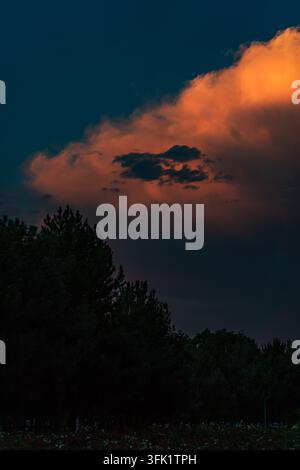Dramatischer Sonnenuntergangshimmel mit dunklen Gewitterwolken, die lebendige orange und rote Wolken überlagern. Stockfoto