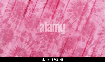 Eine Nahaufnahme eines weichen rosa Batikstoffs mit einem sich wiederholenden kreisförmigen Sternburst-Muster und einer zarten, plissierten und körnigen Textur. Stockfoto