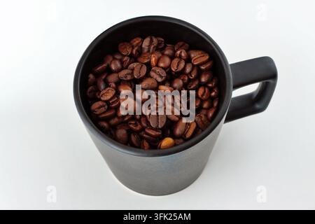 Mainz, Rheinland-Pfalz, Deutschland: Geröstete Kaffeebohnen füllen eine schwarze Keramiktasse auf sauberem weißem Hintergrund. Stockfoto