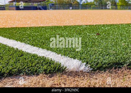 Eine strahlend weiße Grenzlinie schneidet sich durch das lebendige grüne Kunstrasengelände eines professionellen Sportfeldes unter hellem Tageslicht. Stockfoto