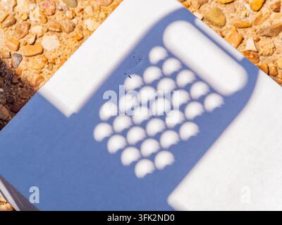 Ein geometrischer Schatten mit kreisförmigen Mustern erstreckt sich über einen sauberen weißen Hintergrund, der auf einem Bett aus kleinen Kieselsteinen ruht. Stockfoto
