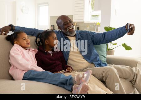 Afroamerikanische Familie mit Senior und Kindern, die auf dem Sofa mit einem Smartphone-Remote ein Selfie machen Stockfoto
