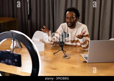 Afroamerikanischer Mann spricht und gestikuliert an einem Studiotisch und trägt einen gestreiften Pullover mit Ringlicht Stockfoto