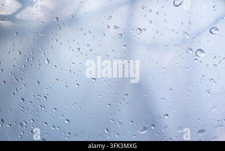 Regentropfen auf einem transparenten Glasfenster mit sanft verschwommenen Schatten und kühlen blaugrauen Regenschattierungen. Stockfoto
