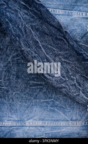 gefalteter blauer Denimstoff mit sichtbaren Falten, Nähten, verblassten Indigotönen und robuster Textur Stockfoto