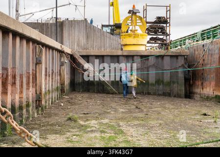 Ein Paar geht Hand in Hand über den freiliegenden Meeresboden bei Ebbe neben Mike's Boatyard in Old Leigh, Leigh-on-Sea. Stockfoto