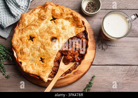 Rindfleisch-Pastete mit dunkler Biersauce und knusprigem Blätterteigboden auf Holzunterlage, Ansicht von oben, Platz für Text. Hausgemachtes Fleischbier-Pastetenrezept. Stockfoto