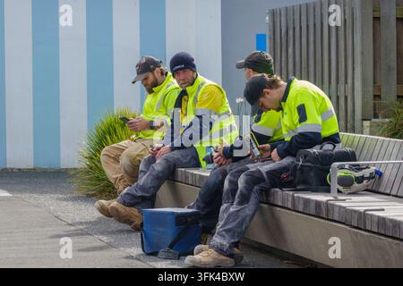 Tauranga, Neuseeland - 26. August 2026; Vier Männer in gelber Sicherheitskleidung sitzen auf einer Bank Stockfoto