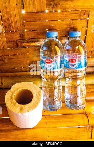 Einfaches thailändisches Bambushütteninterieur, das für Gäste mit Flaschenwasser und ordentlich angeordnetem Toilettenpapier vorbereitet ist, was eine praktische und einladende Atmosphäre schafft Stockfoto
