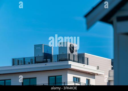 Dachlüftungs-Kondensatoreinheiten und Wärmepumpen auf dem Dach eines modernen Wohngebäudes vor blauem Himmel in Vancouver, British Columbia. Stockfoto