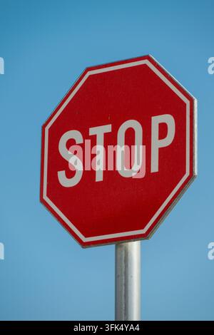 Ein normales rotes achteckiges Stoppschild, das auf einem Metallpfahl montiert ist, hebt sich scharf gegen einen klaren blauen Himmel ab. Stockfoto