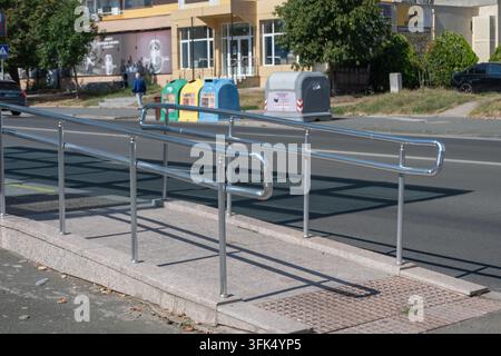 Eine Beton-Zugangsrampe mit glänzenden Edelstahl-Geländern führt sicher zu einem städtischen Fußgängerweg neben einer Stadtstraße. Stockfoto