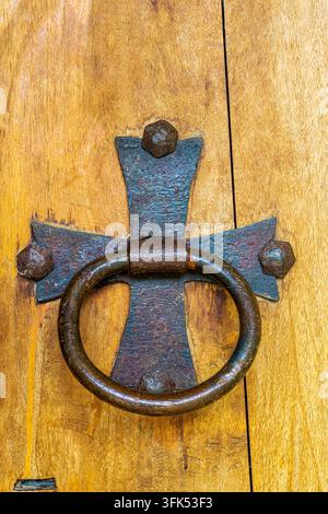 Ein rostiger Eisenschlagring ist an einem Metallkreuz mit Nieten an den Enden befestigt. Die Tür ist aus hellem Holz. Die Texturen sind deutlich sichtbar. Stockfoto