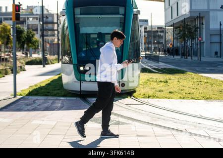Junger Mann überquert Gleise mit Telefon und ignoriert die Straßenbahn Stockfoto