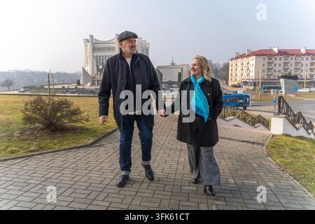 Reifes Paar hält sich an den Händen und spaziert durch die Stadt in der Nähe historischer Architektur, lächelnd an einem sonnigen Tag während eines romantischen Stadtspaziergangs. Stockfoto