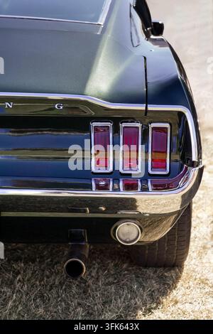 Nahaufnahme der Rückseite eines Ford Mustang, die seine drei vertikalen Rücklichter, den Chromstoßstangenbefestigung, den Auspuffrohr, das Hinterrad und die glänzende dunkle Karosserie zeigt. Stockfoto