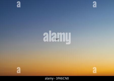 Minimalistische Niedrigwinkelansicht eines Verkehrsflugzeugs, das durch einen klaren, sich verlaufenden Sonnenuntergangshimmel fliegt. Stockfoto