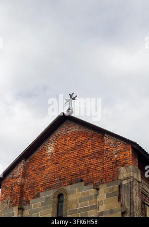 Niedrigwinklige Ansicht der Ziegelfassade und des dekorativen eisernen Kreuzes auf dem Dach einer Kirche. Stockfoto