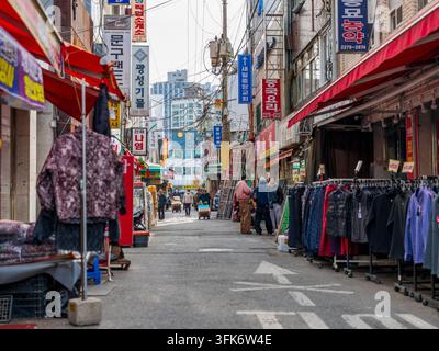 Busan, Busan, Südkorea - 09. Februar 2026: Blick auf einen geschäftigen Straßenmarkt in Busan mit Kleiderständern, farbenfrohen Schildern und Menschen, die entlanggehen Stockfoto
