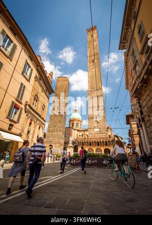 Bologna, Italien - 17. Mai 2018: Blick auf die beiden Türme, Asinelli und Garisenda, die über der historischen Straße aufragen, mit Fußgängern und einem Radfahrer unter einem Stockfoto