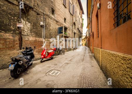 Bologna, Italien - 17. Mai 2018: Blick auf eine schmale Kopfsteinpflasterstraße in Bologna, Italien, mit historischen Backsteingebäuden, einem geparkten roten Roller und einem M Stockfoto