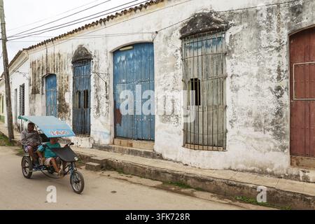 Remedios, Villa Clara, Kuba - 28. Februar 2020: Blick auf einen Mann, der ein Pedal-Taxi entlang einer Straße mit verwitterten weißen Wänden, blauen Türen und Eisen... Stockfoto