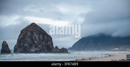 Haystack Rock am Cannon Beach mit einem Weitwinkelblick auf die umliegenden Strände und die Berge im Hintergrund an einem bewölkten Tag. Stockfoto