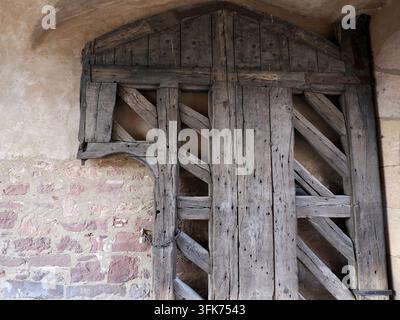 Verwitterte mittelalterliche Holztür mit diagonaler Verstrebung, eingebaut in ein steinernes Bogentor der Burg Steinau, Deutschland. Stockfoto