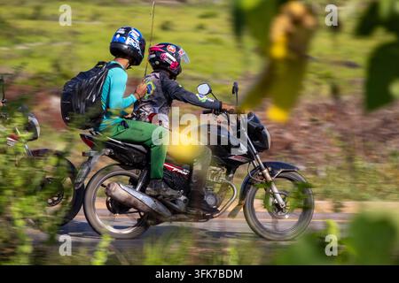Zwei Personen, die von einem Angelausflug zurück nach Hause kommen, auf einem schwarzen Motorrad vor einem grünen verschwommenen Hintergrund Stockfoto