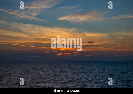 Farbenfroher Sonnenaufgang über dem Meer mit glühenden orangefarbenen Wolken und feinen Zirruswolken vor dem frühmorgendlichen Himmel. Stockfoto