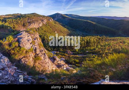 Eine malerische Luftaufnahme zeigt schroffe felsige Klippen und weite, sanfte grüne Hügel unter einem hellen Himmel während einer Wanderung in Portugal. Stockfoto