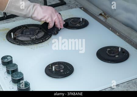 Eine Hand in einem rosa Gummihandschuh wischt mit einem Schwamm einen gläsernen Gasherd ab. Stockfoto