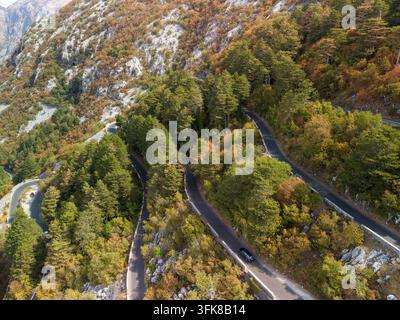 Lovcen Serpentine Montenegro: Die Serpentinenstraße schlängelt sich durch dichten Wald und felsiges Berggelände. Die sich windende Asphaltstraße biegt um Klippen und Herbstnebel Stockfoto