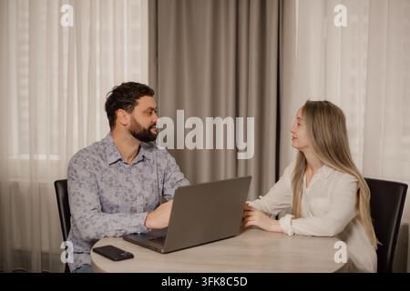 Mann mit Laptop bei einem Vorstellungsgespräch oder einer geschäftlichen Beratung mit einer jungen Frau am Tisch Stockfoto
