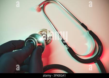 Hand hält ein Stethoskop vor einer Bitcoin-Münze, symbolisch für die finanzielle Gesundheitsanalyse von Kryptowährungen Stockfoto