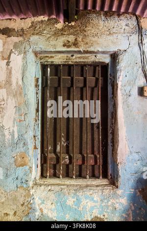 altes Holzfenster mit rostigen Eisenstäben an einer abblätternden blauen Wand, verwitterte Textur und rissige Lackoberfläche, rustikaler architektonischer Hintergrund Stockfoto