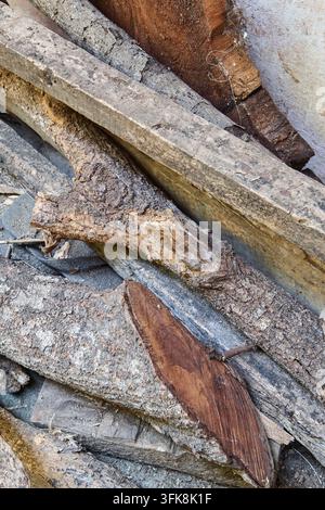 Haufen alter Holzstämme und Holzplanken auf dem Boden, raue Rindenstruktur und verwitterte braune Holzstücke, weiche Fokus rustikales Zimmermannsmaterial Stockfoto
