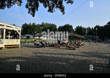 • Sommerfeste am Strand – Urlauber ruhen sich im Schatten von Strohdächern aus Stockfoto
