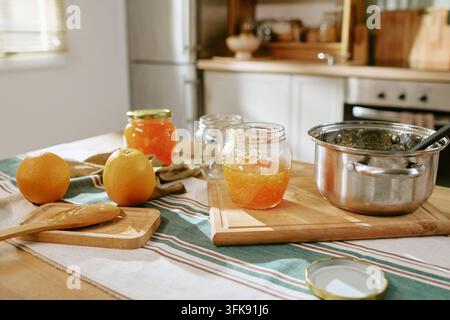Hausgemachte Orangenmarmelade in Gläsern, die auf dem Küchentisch zubereitet wird Stockfoto