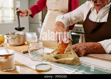 Seniorenpaar stellt hausgemachte Marmelade und Einmachgläser in der Küche her Stockfoto