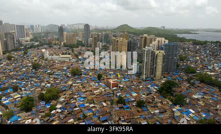 Luftbild der Dharavi-Slums mit dichter niedriger Bebauung und blauen Planendächern, die sich von modernen Hochhauswohnungen in Mum abheben Stockfoto