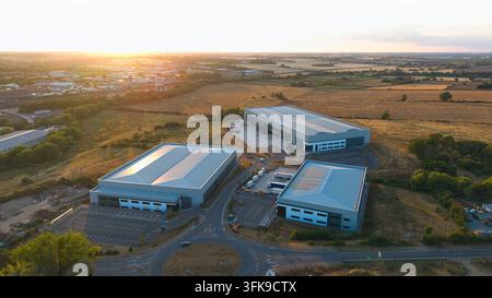 Luftaufnahme moderner Industriehallen, umgeben von Feldern, im warmen Licht des Sonnenuntergangs in Wellingborough, England, Vereinigtes Königreich. Stockfoto