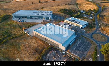Luftaufnahme von Industriegebäuden, umgeben von Feldern und einem Kreisverkehr im goldenen Abendlicht in Wellingborough, England, Vereinigtes Königreich. Stockfoto