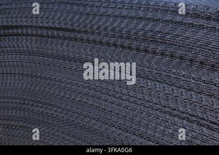 Abstrakte Nahaufnahme von gestapelten galvanisierten Stahl Drahtgitter-Paneelen, die ein gebogenes Metallmuster im Freien auf einer Baustelle bilden. Stockfoto
