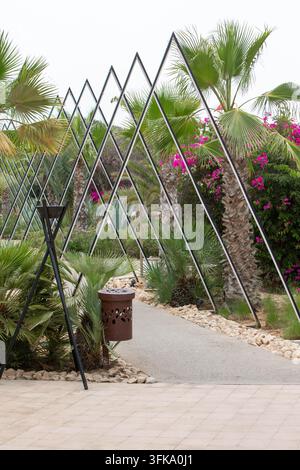 Moderner gestalteter tropischer Gartenweg mit dekorativen Metallbögen und Palmen in einem Luxusresort. Schön gestalteter tropischer Garten mit Stockfoto